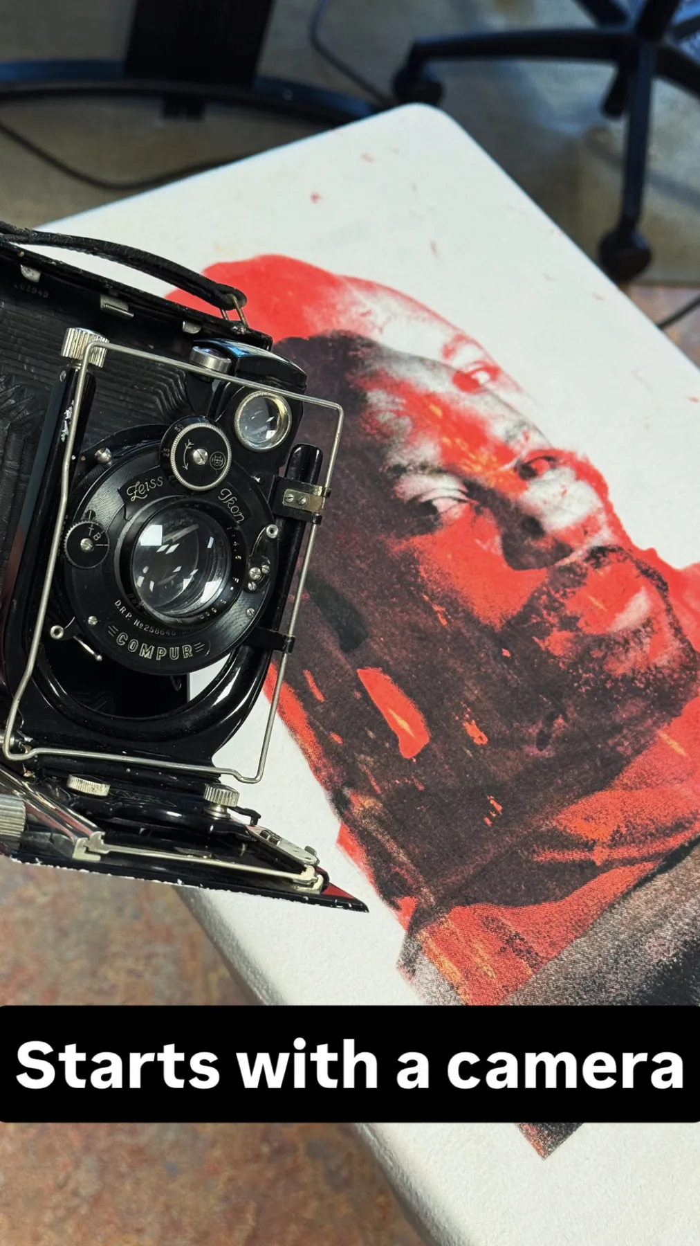Large format camera placed next to a red and black portrait print